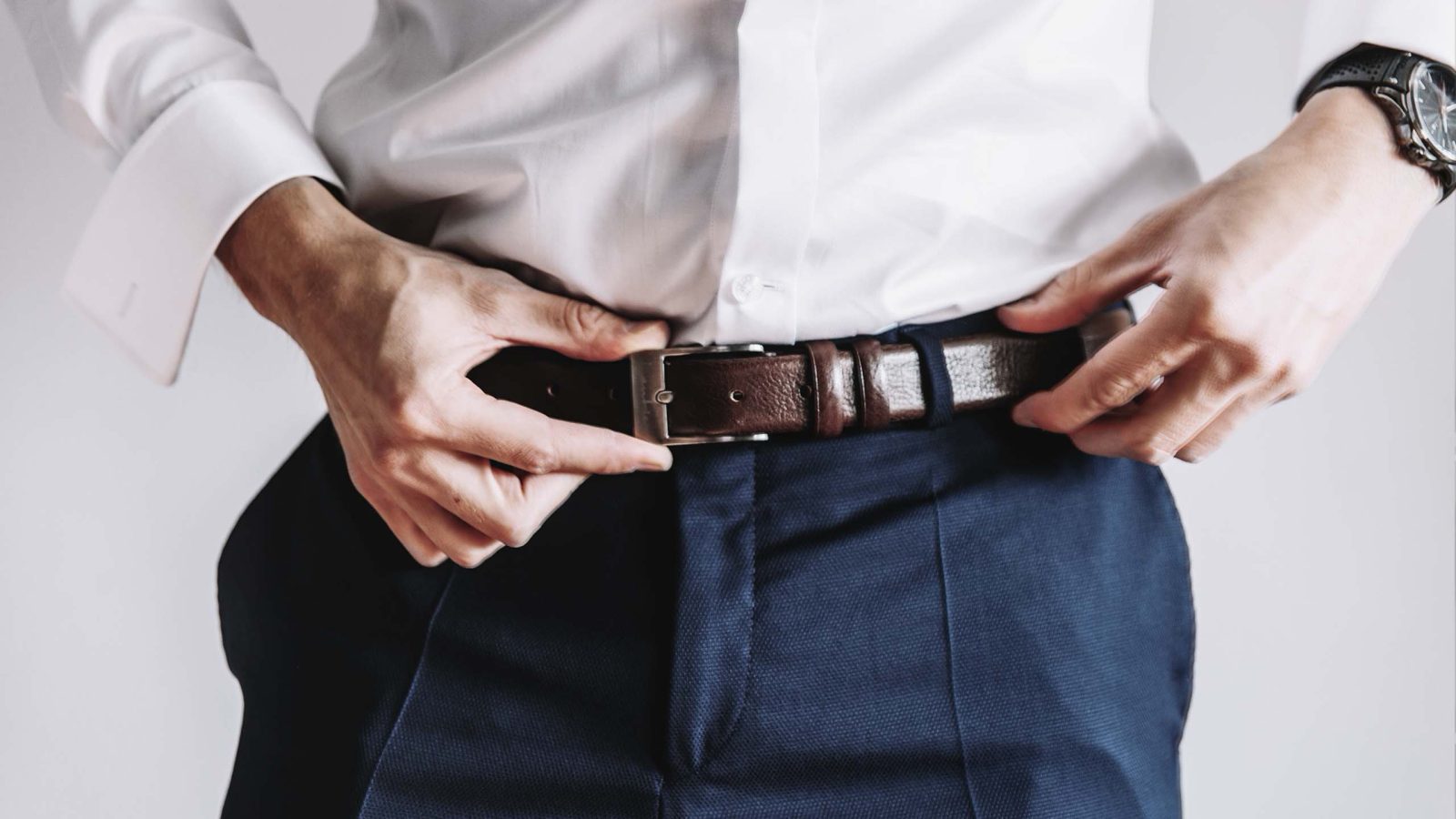 Loslassen – Mann mit blauer Anzugshose und weißem Hemd. Durch einen braunen Gürtel wird die Hose gehalten.